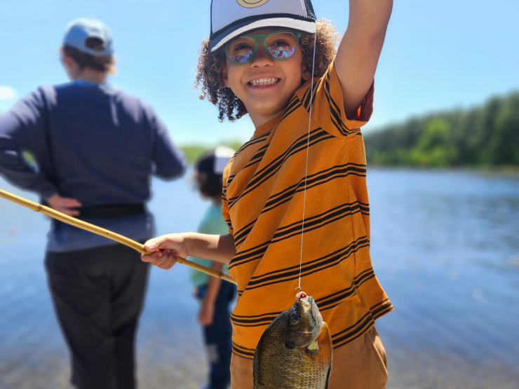 kid holding up a fish in front of a lake