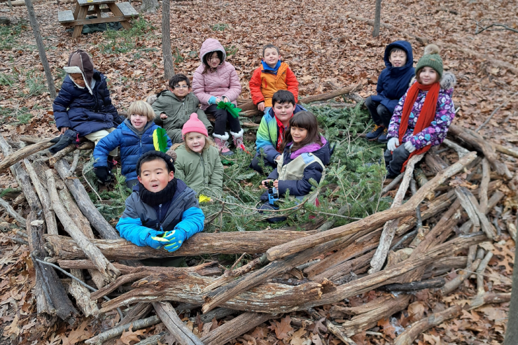 kids sitting in a fort of sticks and pine branches